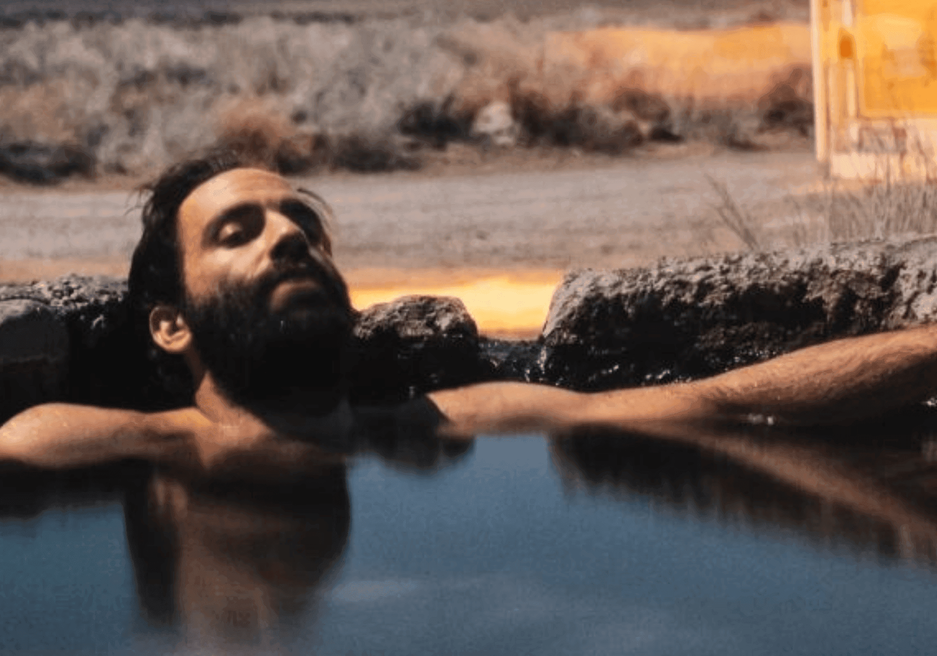 Man in an outdoor hottub with a mountain in the background