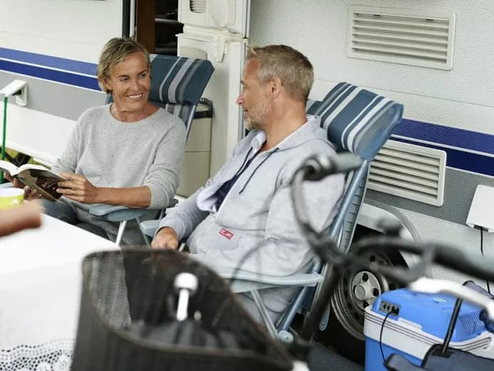 Man and woman sitting in chairs in front of autocamper